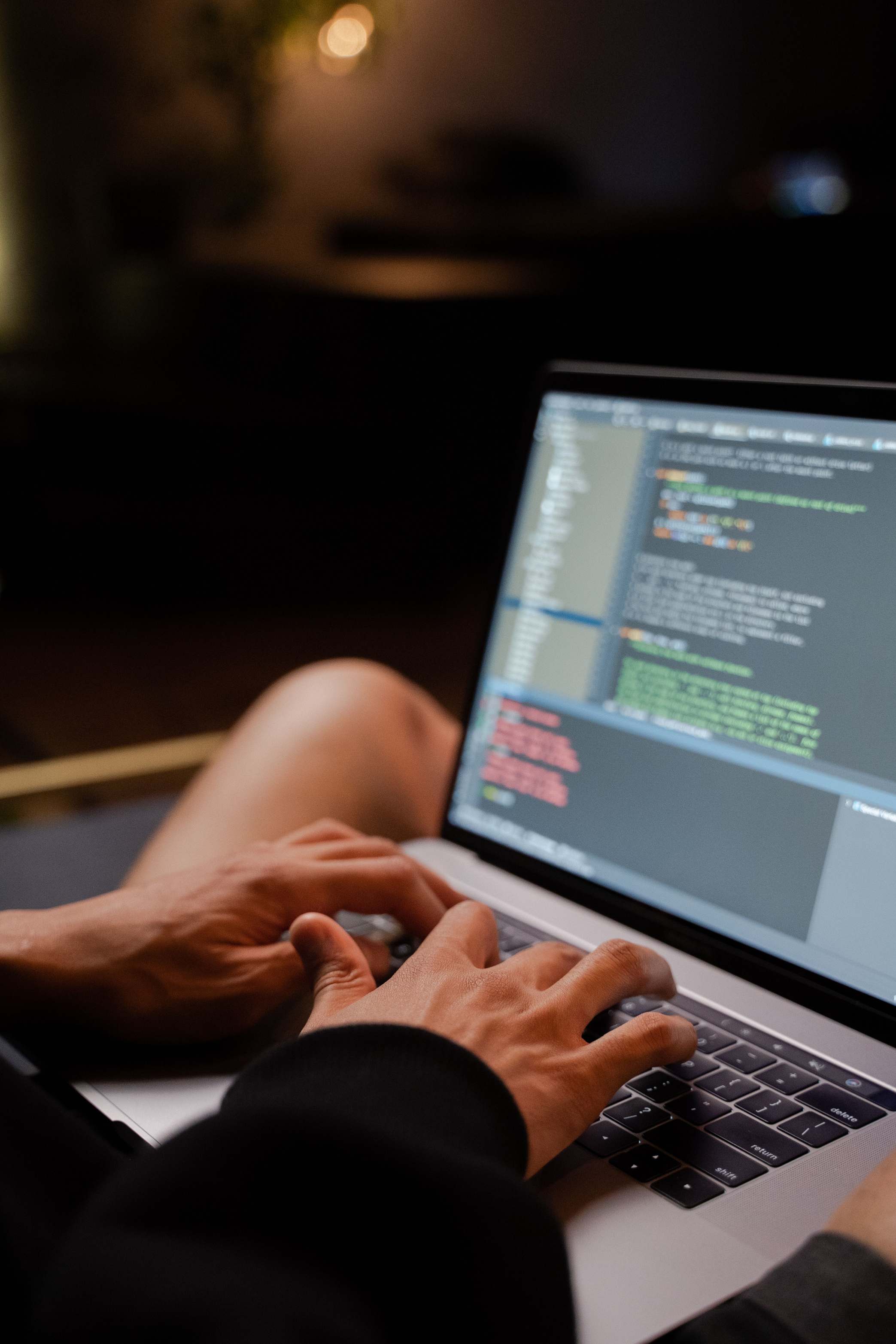 Hands typing on a laptop keyboard during software work, programmer typing code in a dimly lit room